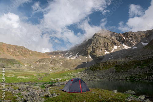 Tourist tent stands next to a high-mountain lake on the background of Mount Dzhalkaush, height 3283, Teberda, Karachay-Cherkessia, Russia