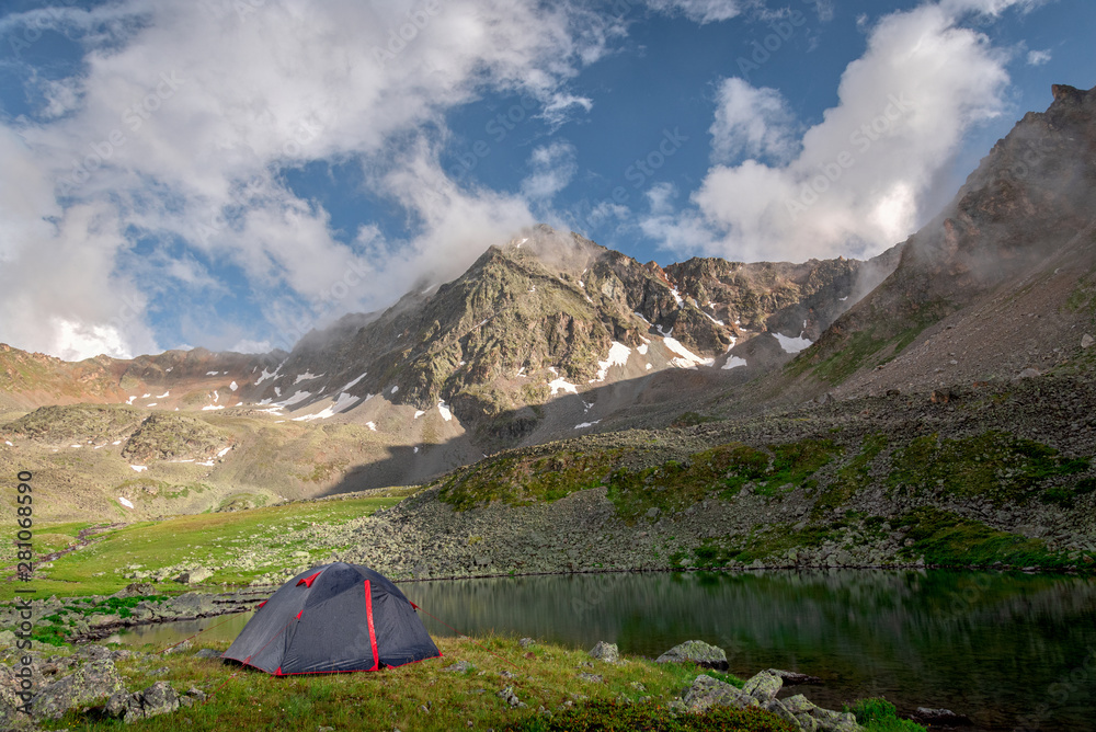 Tourist tent stands next to a high-mountain lake on the background of Mount Dzhalkaush, height 3283, Teberda, Karachay-Cherkessia, Russia