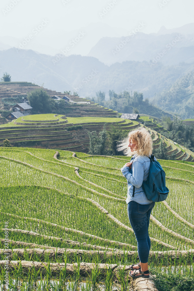 Young Caucasian blonde woman in denim shirt overlooking Sapa rice terraces at sunset in Lao Cai province, Vietnam