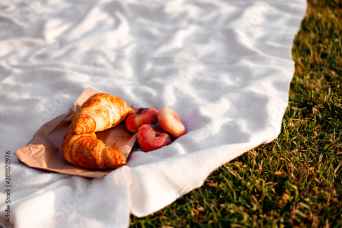 Croissants and fig peaches on a white plaid lie on the grass. Picnic on a sunny day.