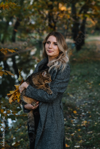 girl and a cat in the autumn park.a woman in a brown sweater walking with her gray cat in an autumn park