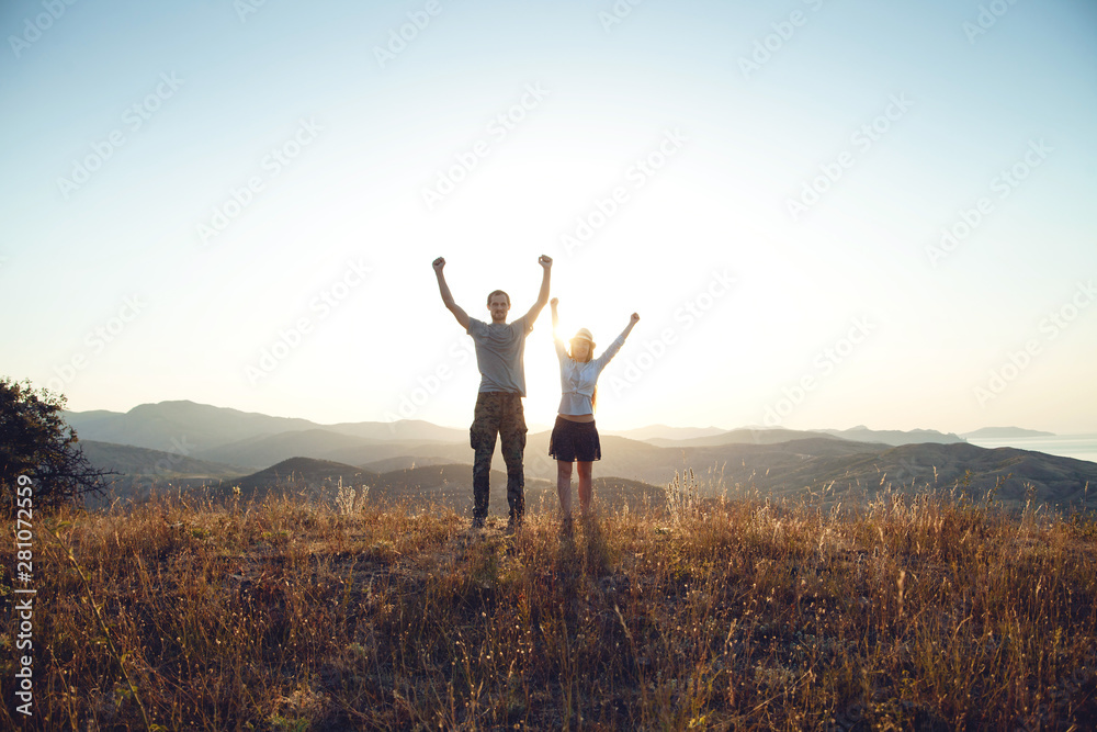 A young couple raise their arms in a victorious gesture. Dawn in the mountains, the beginning of a new day A young couple raise their arms in a victorious gesture. Dawn in the mountains, the beginning of a new day
