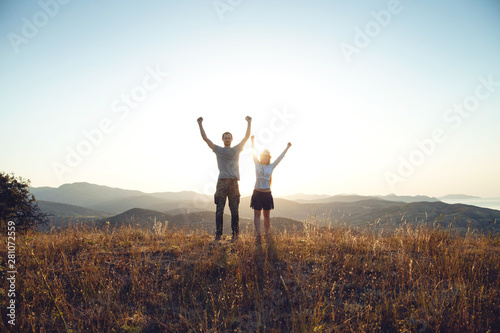 A young couple raise their arms in a victorious gesture. Dawn in the mountains, the beginning of a new day
