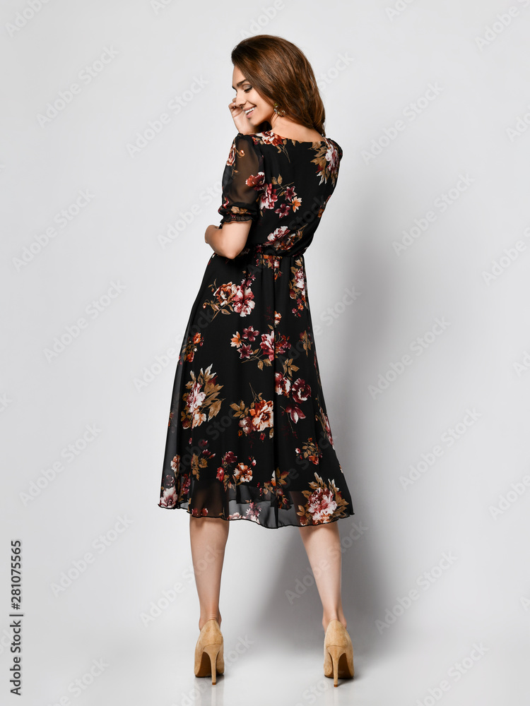 Fototapeta premium Slim curly female model in a silk pale dark dress looking at the camera in full growth. Cute girl in romantic clothes is going on a date