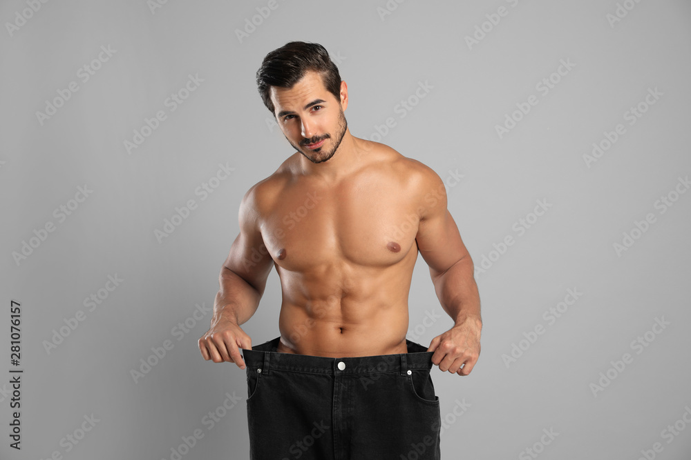 Young man with slim body in old big size jeans on grey background