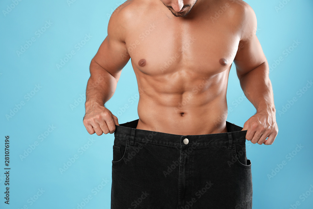 Young man with slim body in old big size jeans on light blue background, closeup view Young man with slim body in old big size jeans on light blue background, closeup view