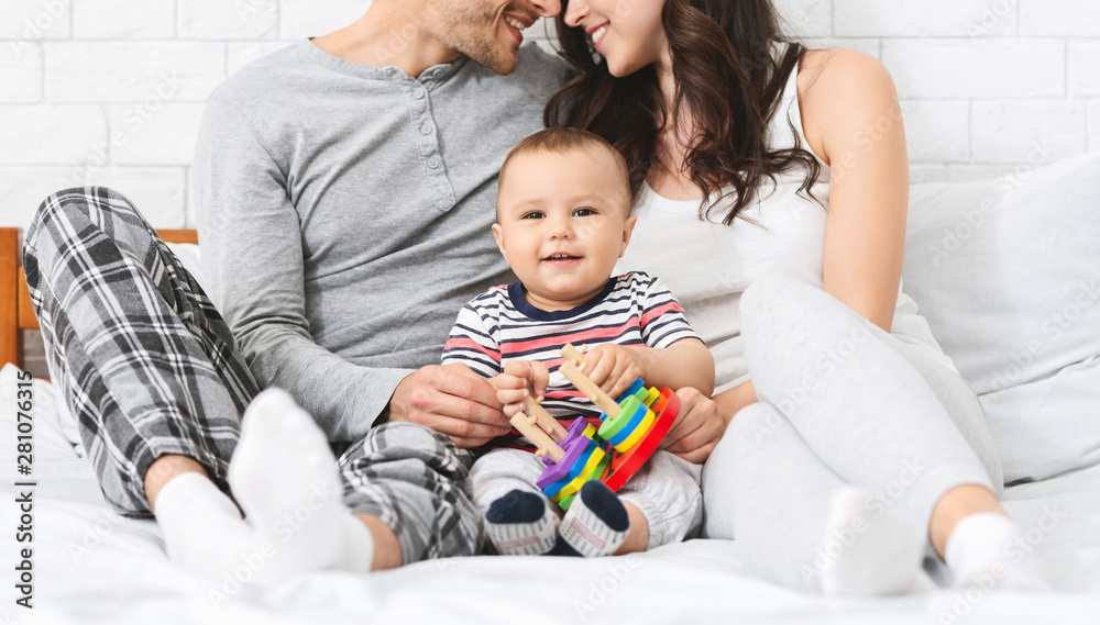 Sweet little baby smiling, sitting on bed with loving parents Sweet little baby smiling, sitting on bed with loving parents