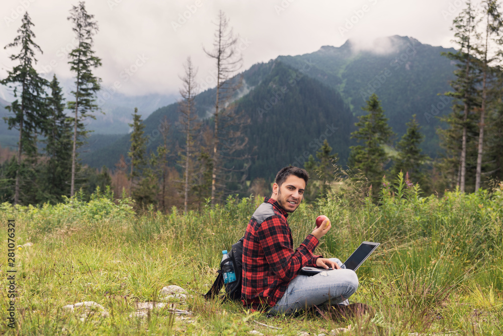 Young brunette male in jeans and shirt is working at a computer while being on the nature. The concept of work on freelancing. Young brunette male in jeans and shirt is working at a computer while being on the nature. The concept of work on freelancing.