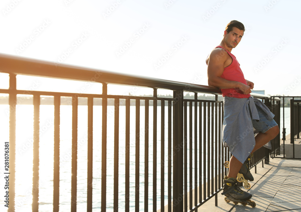 Handsome young man with roller skates on pier near river, space for text