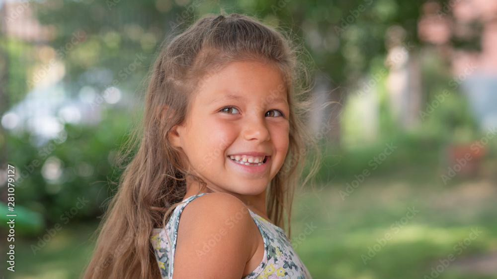 Authentic shot of cute little girl with loose hair is smiling in camera outside her house on a sunny day. Authentic shot of cute little girl with loose hair is smiling in camera outside her house on a sunny day.