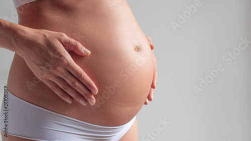Wallpaper Mural Authentic close up shot of an young pregnant woman in cosy underwear is caressing her belly isolated on a white background. Torontodigital.ca