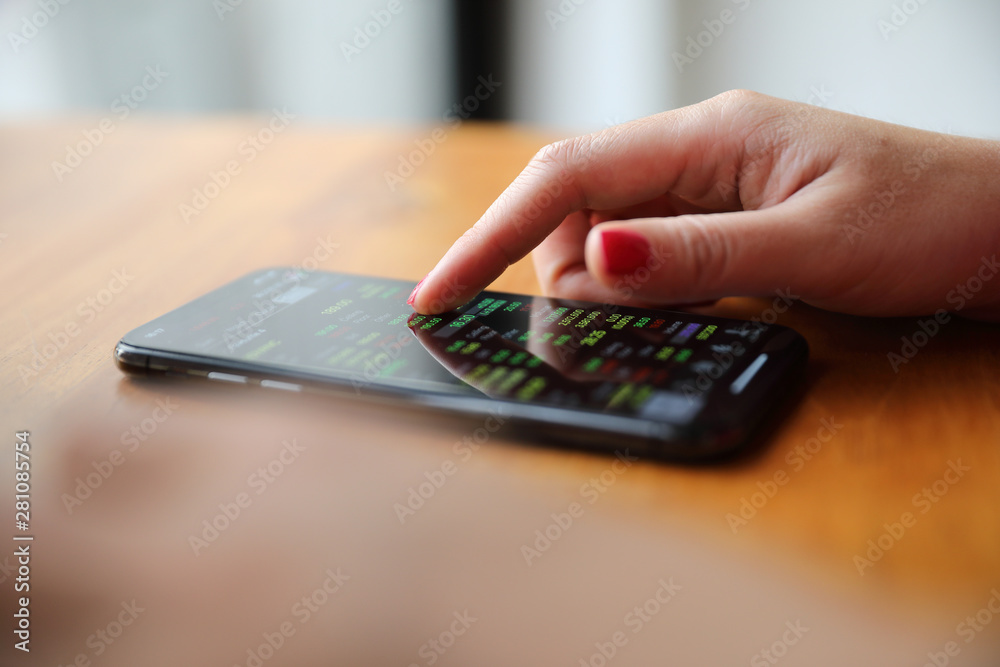 Female hand with smartphone trading stock online in coffee shop , Business concept Female hand with smartphone trading stock online in coffee shop , Business concept