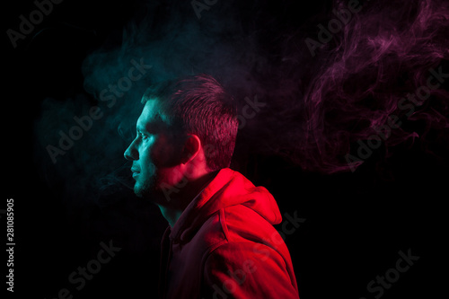 Portrait of a man in profile face looking towards a black isolated background with a sense of hope and dreaming, around head a cloud of blue and pink smoke. The soul and feelings of man.