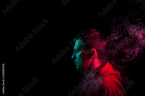 Portrait of a man in profile face looking on a black isolated background with a feeling of sadness and loneliness, around the head a cloud of blue and pink smoke. The soul and feelings.