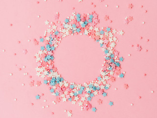 Festive border frame of colorful pastel sprinkles on pink background with copy space in center. Sugar sprinkle dots and stars in round shape, decoration for cake and bakery. Top view or flat lay