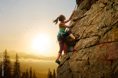 Beautiful Woman Climbing on the Rock at Foggy Sunset in the Mountains. Adventure and Extreme Sport Concept