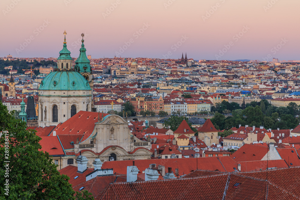 View over Prague from the district Lesser Town with stairs from the Prague Castle with alley, historical buildings and trees in the evening. View over rooftops of Pragues Old Town with churches