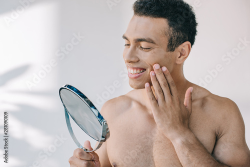 Bild auf Leinwand handsome mixed race man touching face with hand while looking at mirror