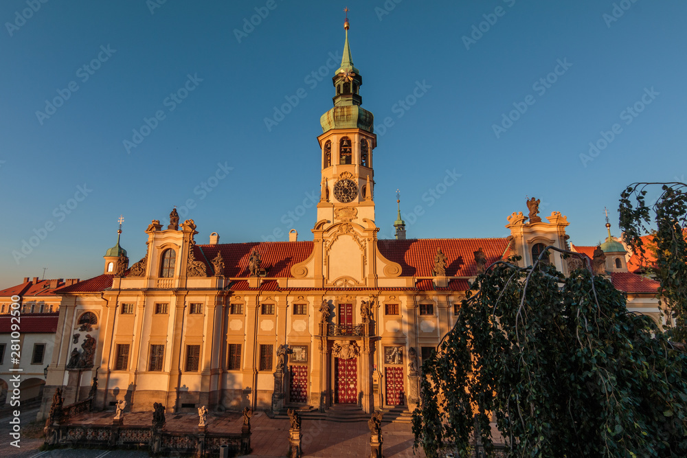 Obraz premium Direct view of the historic Baroque building complex in the Czech capital of in the evening sun with blue sky. Capuchin Church Loreta from Hradcany Square near the Prague Castle