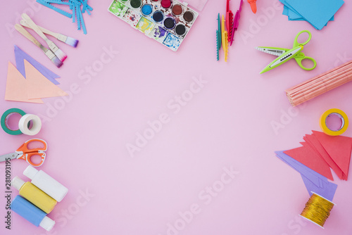 Paintbrush; color palette; scissor; golden spool; paper and scissor on pink backdrop