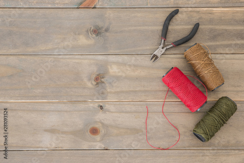 An overhead view of pliers and colorful yarn spools on wooden desk