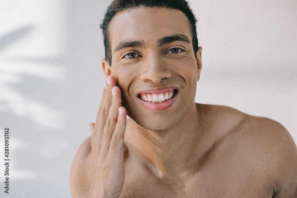 portrait shot of handsome mixed race man touching cheek while smiling and looking at camera portrait shot of handsome mixed race man touching cheek while smiling and looking at camera