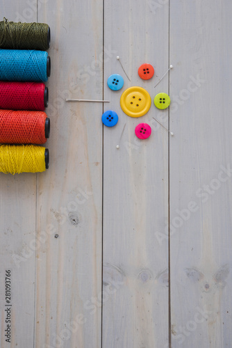 Colorful yarn spools with decorative needles; pushpins and colorful buttons on wooden desk