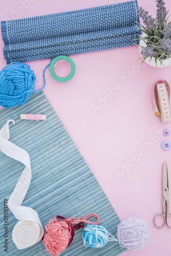 Placemat; ribbon; scissor; spool; measuring tape; button and wool on pink background