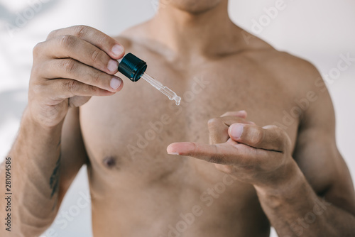 selective focus of mixed race man dropping serum from pipette on finger