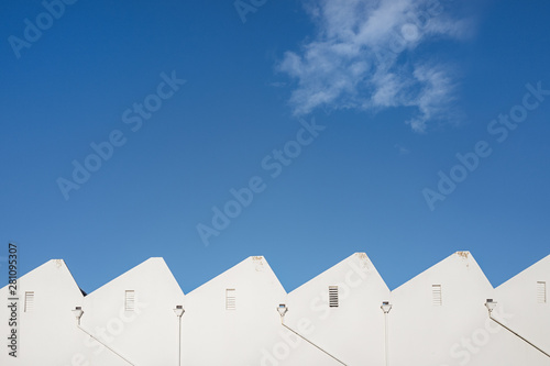 White factory sawtooth roofline against a vivid blue sky