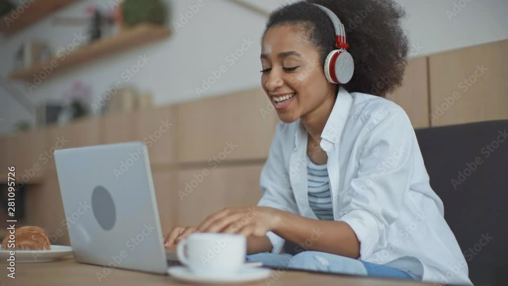 young, cheerful african american businesswoman in headphones having video chat on laptop while sitting in cafe