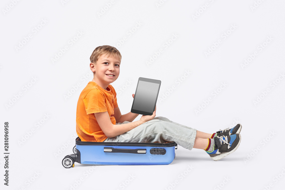 Cheerful boy with tablet sitting in suitcase Cheerful boy with tablet sitting in suitcase