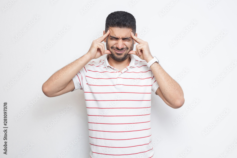 headache or confution. Portrait of confused handsome bearded young man in striped t-shirt standing, holding his painful head or thinking. indoor studio shot, isolated on white background. headache or confution. Portrait of confused handsome bearded young man in striped t-shirt standing, holding his painful head or thinking. indoor studio shot, isolated on white background.