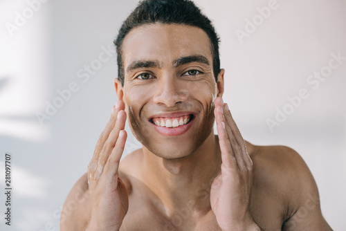 handsome young man with wet face touching it with hands while smiling and looking at camera