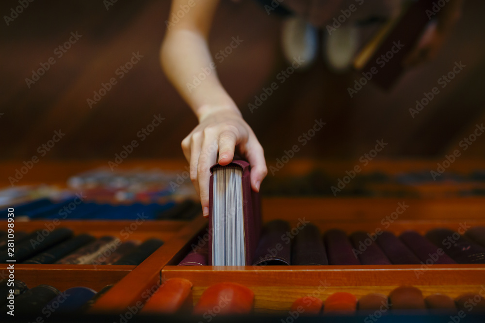 © Bonninstudio/Stocksy - Close up of student's hand placing book on shelf in library