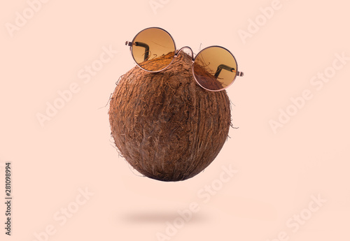 Coconuts are wearing sunglasses over pink background. Concept vacation in the sunny tropics, levitating coconut with glasses