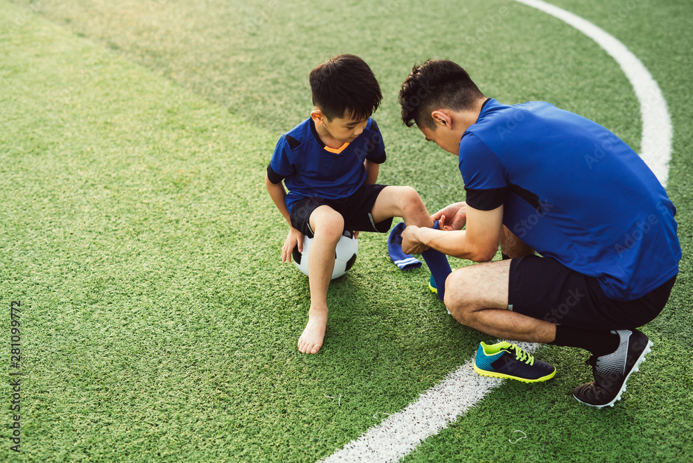 © MaaHoo Studio/Stocksy - Father putting socks on his son on soccer field © MaaHoo Studio/Stocksy - Father putting socks on his son on soccer field