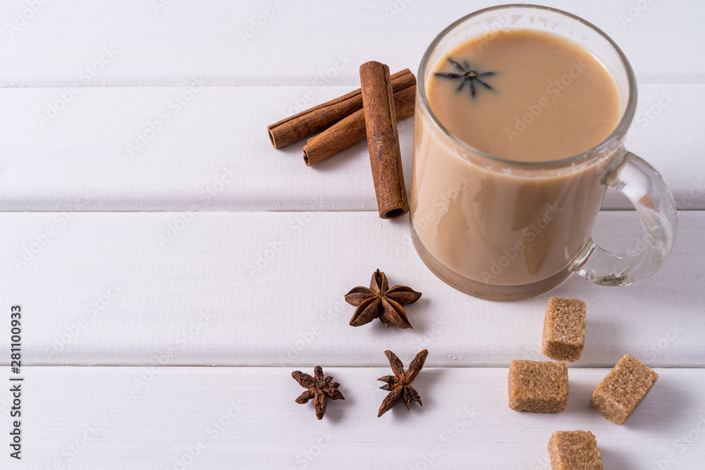 Masala chai tea in a mug, brown sugar, cinnamon sticks, anise over white table background.