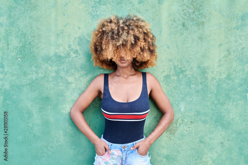 Woman covering her face with hair standing by wall