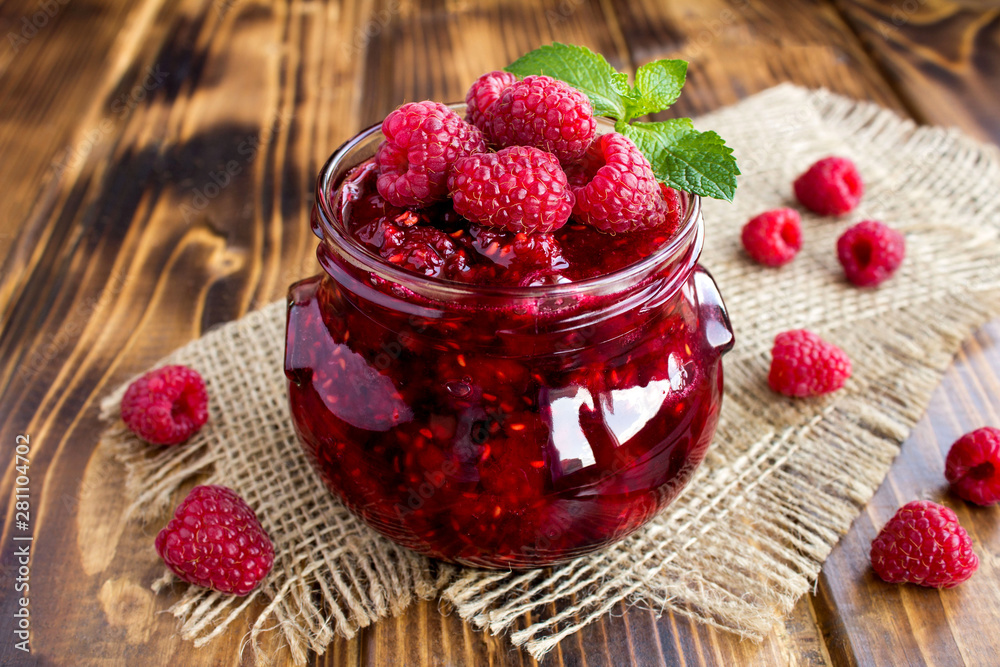 Raspberry  jam in the glass jar on the rustic brown wooden  background. Closeup.