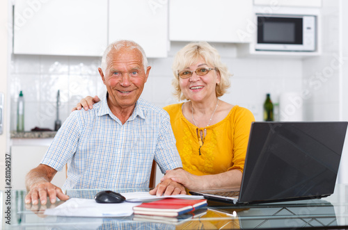 Smiling mature family couple sitting at laptop at kitchen table