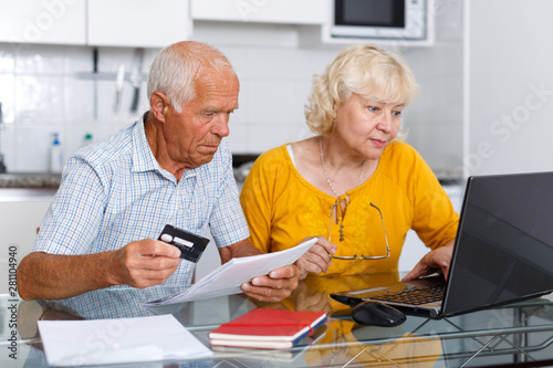 Senior man and woman with banking card near laptop together
