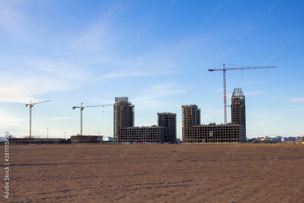 tower cranes build skyscrapers in the sandy desert against the city under a blue sky tower cranes build skyscrapers in the sandy desert against the city under a blue sky