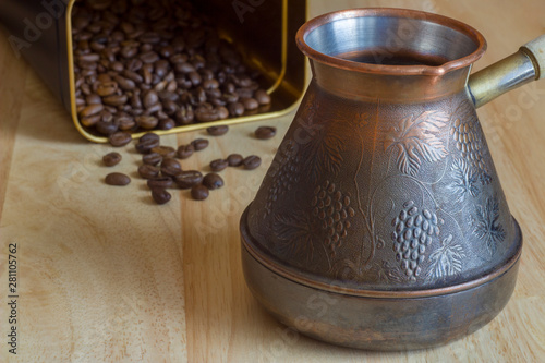 yellow copper turk coffee maker on a blurred background of the wooden surface of the table with roasted brown coffee beans