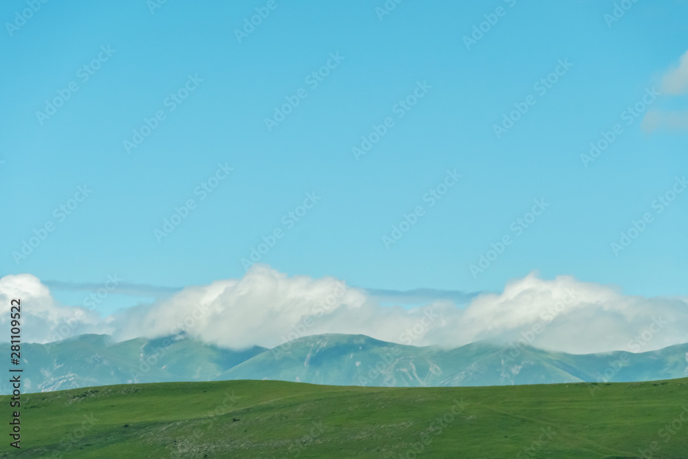 Summer landscape of sky, mountains with clouds, grass on a sleepy day