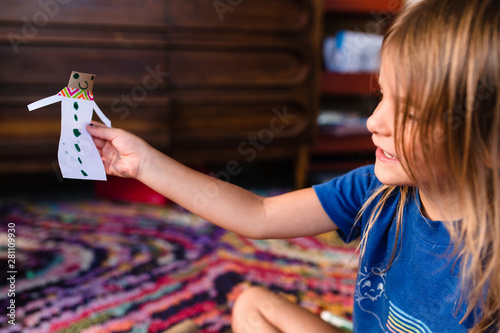 little girl holds up paper doll she made