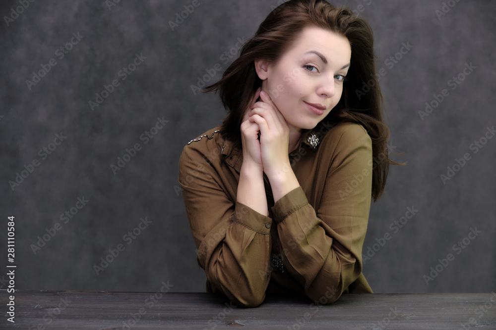 Portrait of a pretty beautiful fashionable adult brunette girl in a dress on a gray background. Sits at the table, talking, bored, showing different poses and emotions Portrait of a pretty beautiful fashionable adult brunette girl in a dress on a gray background. Sits at the table, talking, bored, showing different poses and emotions