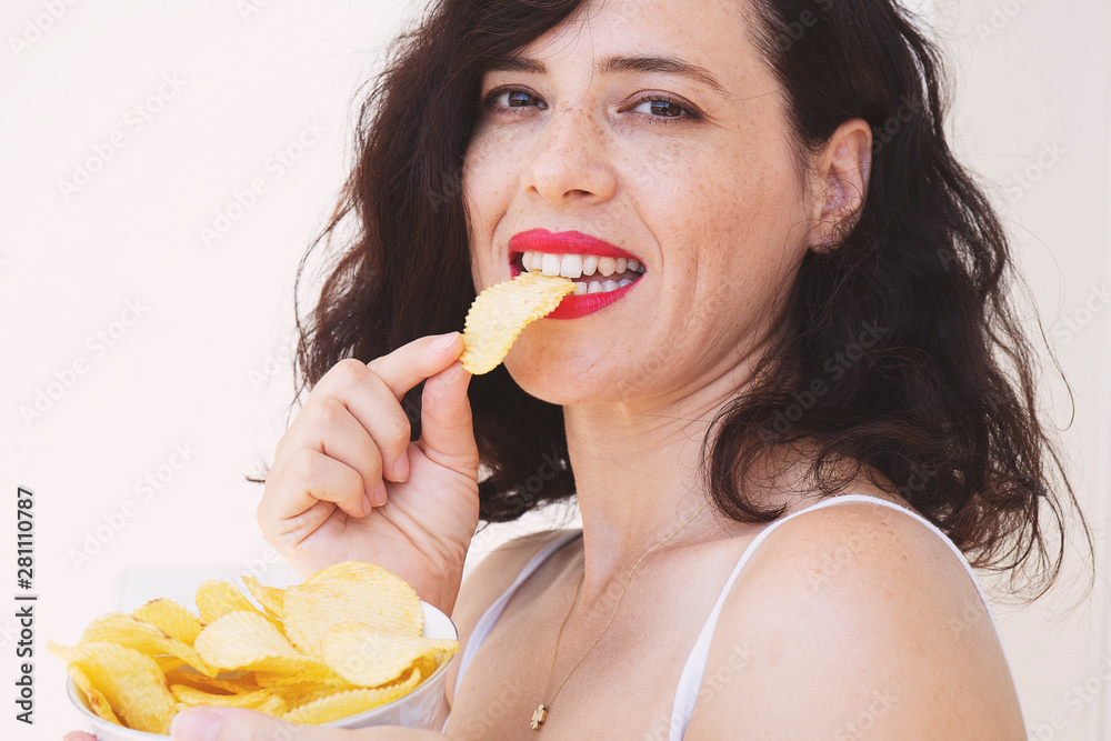 Young woman eating potato chips out of a bowl against a white background Young woman eating potato chips out of a bowl against a white background