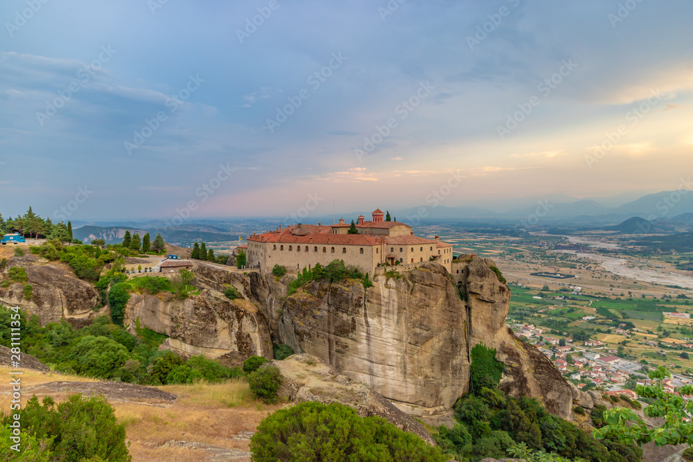 Agios Stephanos or Saint Stephen monastery located on the huge rock with mountains and town landscape in the background at evening. Meteors, Trikala, Thessaly, Greece