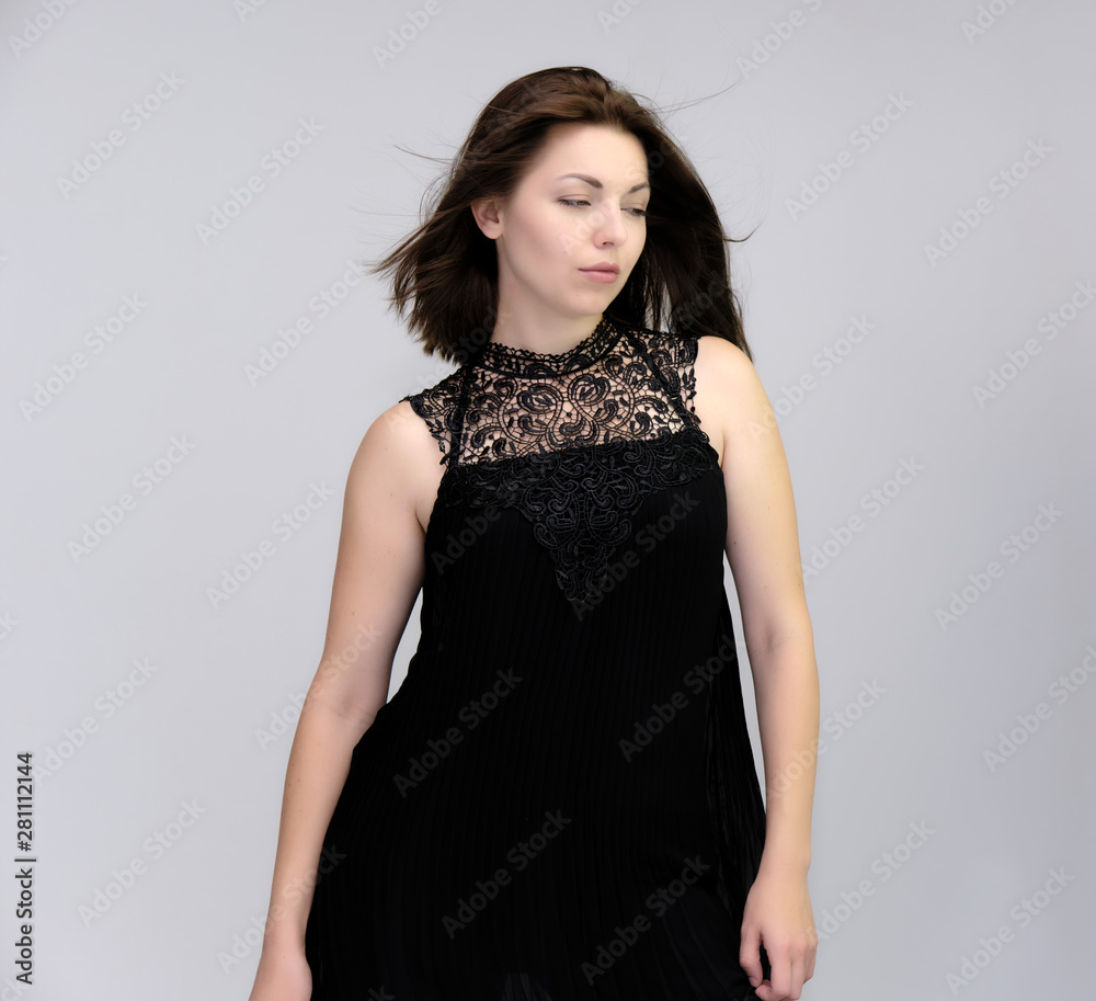 A portrait above the knee of a pretty beautiful fashionable adult brunette girl in a black dress on a white background. Standing right in front of the camera, showing different poses and emotions. A portrait above the knee of a pretty beautiful fashionable adult brunette girl in a black dress on a white background. Standing right in front of the camera, showing different poses and emotions.